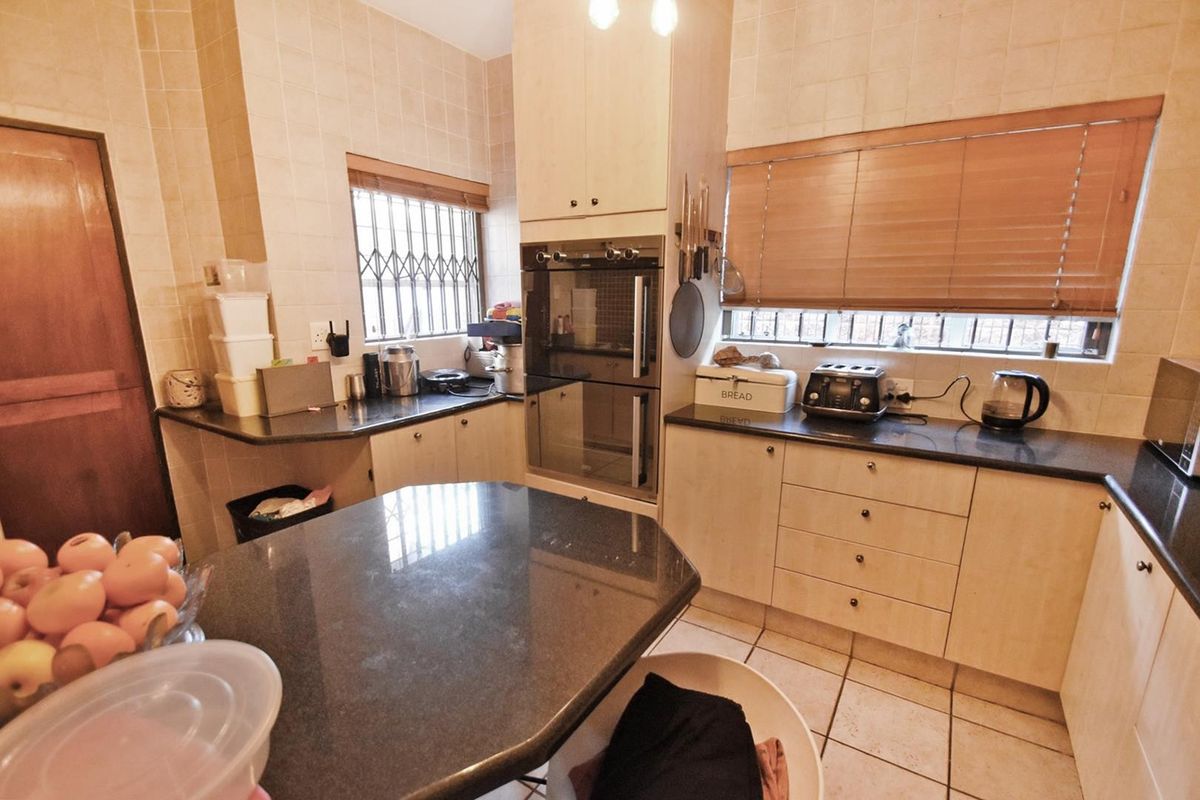 A functional kitchen featuring built-in double ovens, granite countertops, tiled walls, and ample cabinetry, providing a practical workspace with secure window fittings.