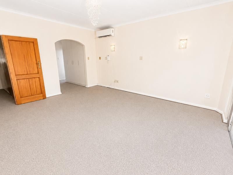 A spacious, empty living room featuring neutral carpeting, a split-system air conditioner, and built-in storage cupboards, offering a clean canvas for interior design.