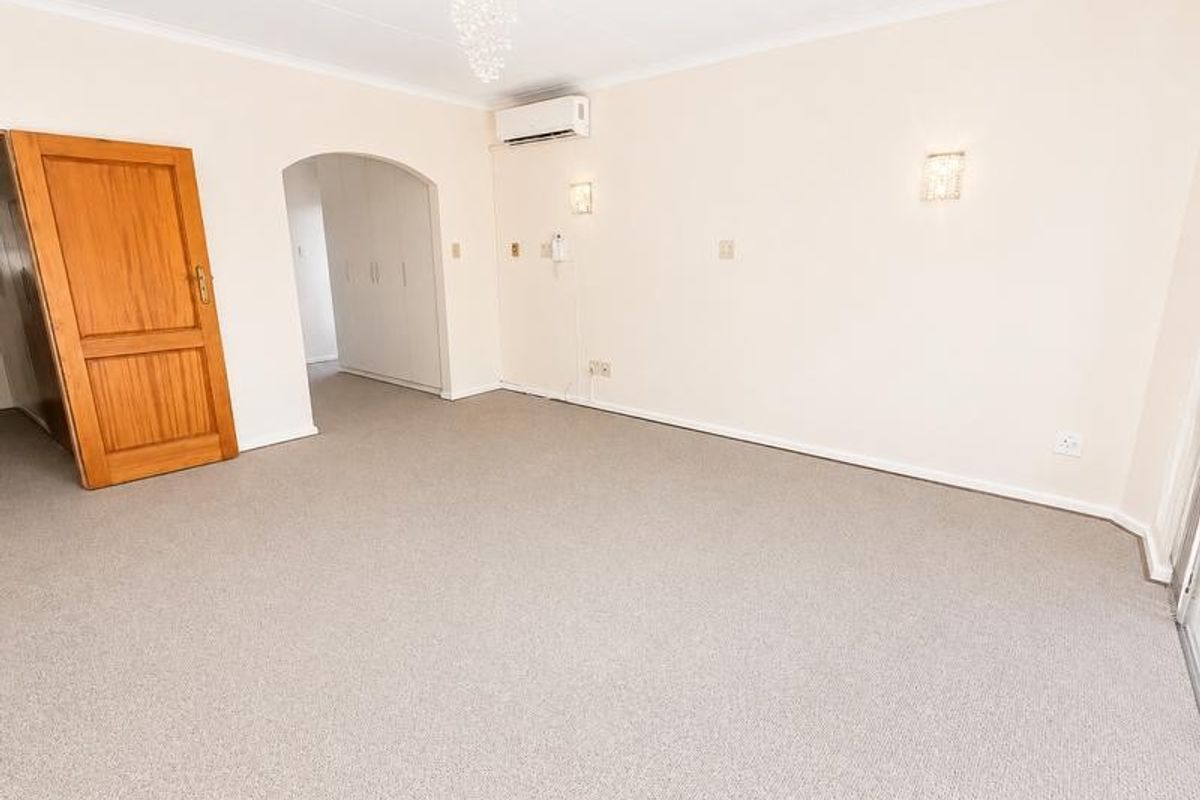 A spacious, empty living room featuring neutral carpeting, a split-system air conditioner, and built-in storage cupboards, offering a clean canvas for interior design.