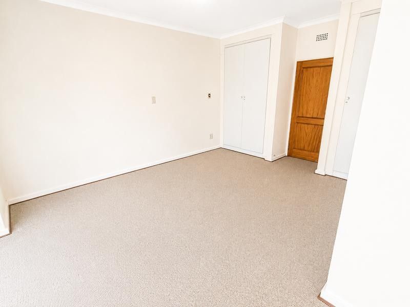 A clean, empty bedroom featuring neutral carpet flooring, built-in wardrobe storage, and a classic timber door.