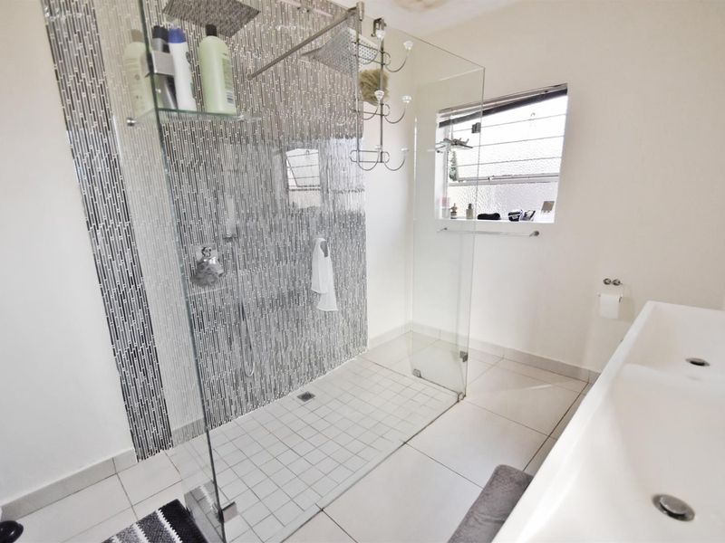 Modern bathroom featuring a spacious walk-in shower with mosaic tile accents, double vanity basin, and a functional louvre window for ventilation.