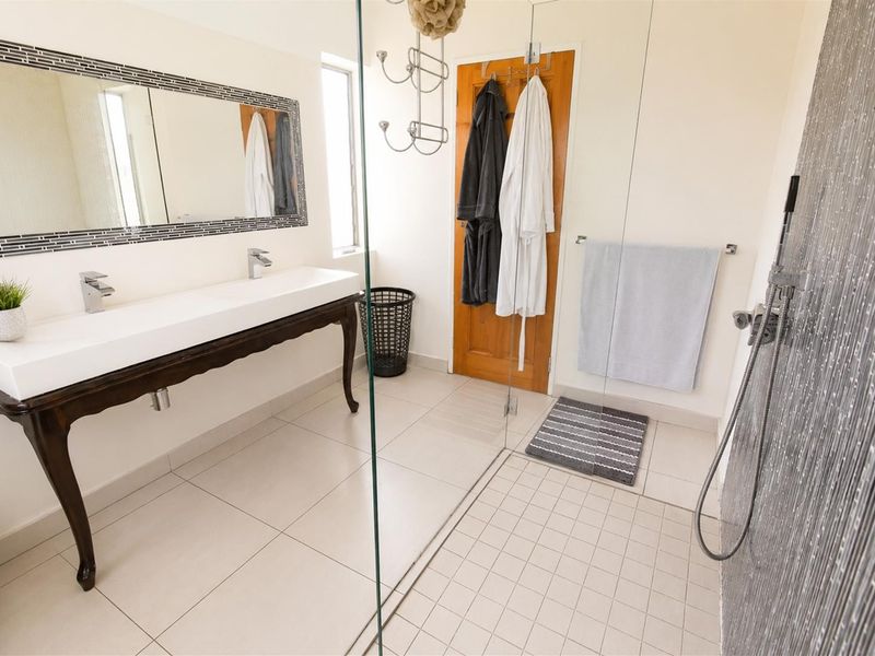 A modern bathroom featuring a double vanity with a decorative mirror, a spacious walk-in shower with a glass screen, and neutral floor tiling.