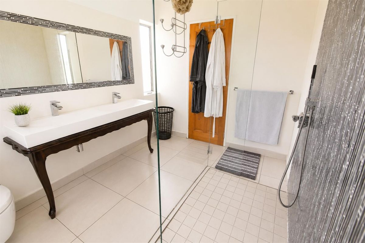A modern bathroom featuring a double vanity with a decorative mirror, a spacious walk-in shower with a glass screen, and neutral floor tiling.