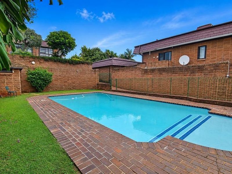 Private outdoor pool area featuring a swimming pool, brick paved surround, and established lawn enclosed by high brick boundary walls.