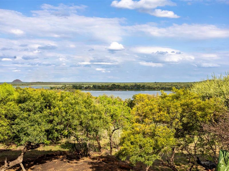 A scenic landscape view overlooking a natural lake and surrounding bushveld vegetation under a clear blue sky.