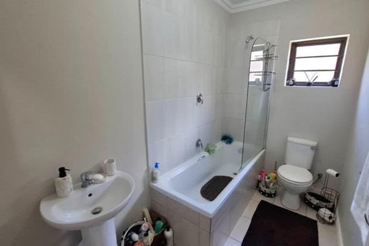 A functional bathroom featuring a pedestal basin, a bathtub with a glass shower screen, and a toilet, finished with neutral wall and floor tiles.