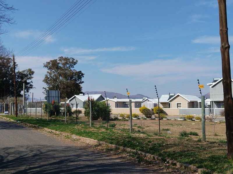Street view of a townhouse complex featuring perimeter electric fencing and visible solar geysers on the roof structures.