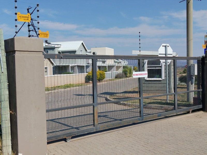 Secure gated entrance to the townhouse complex featuring a sliding security gate, electric fencing, and a dedicated guard booth.