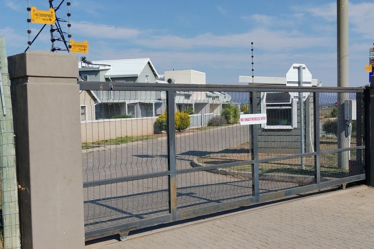 Secure gated entrance to the townhouse complex featuring a sliding security gate, electric fencing, and a dedicated guard booth.