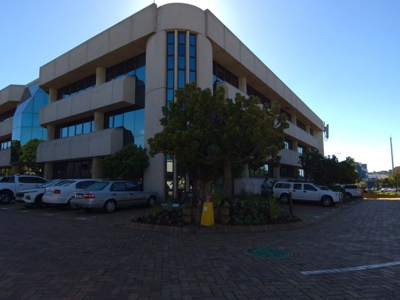 A multi-story commercial office building featuring a concrete facade, tinted glass windows, and an expansive paved parking area.