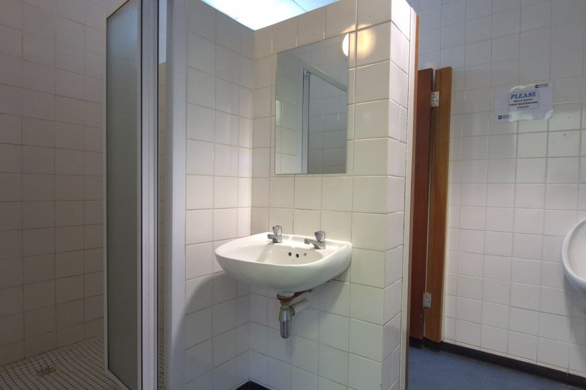 Functional commercial bathroom facility featuring a wall-mounted basin, urinal, and a separate shower cubicle with full-height ceramic wall tiling.