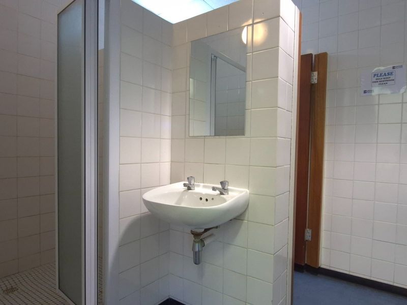 Functional commercial bathroom facility featuring a wall-mounted basin, urinal, and a separate shower cubicle with full-height ceramic wall tiling.