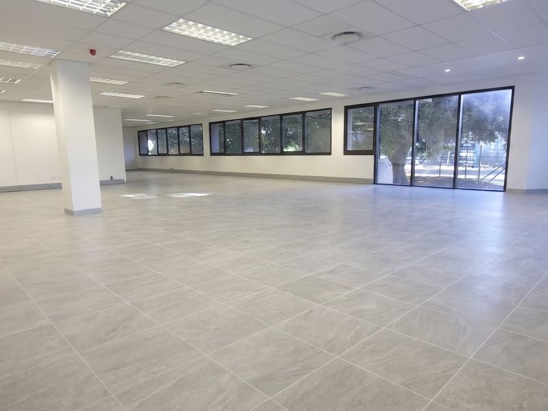 A spacious, open-plan retail or office area featuring modern tiled flooring, a suspended ceiling with recessed lighting, and large windows providing ample natural light.