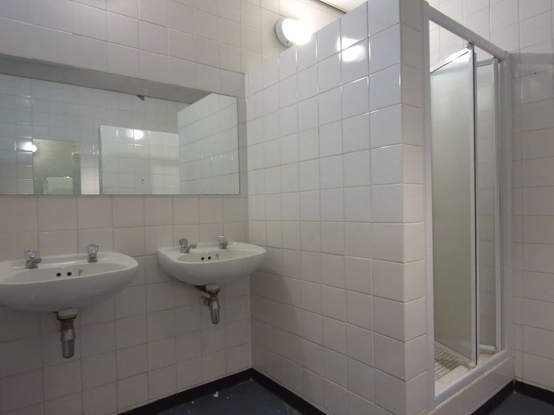Functional commercial bathroom featuring dual wall-mounted washbasins, a shower enclosure, and fully tiled walls.