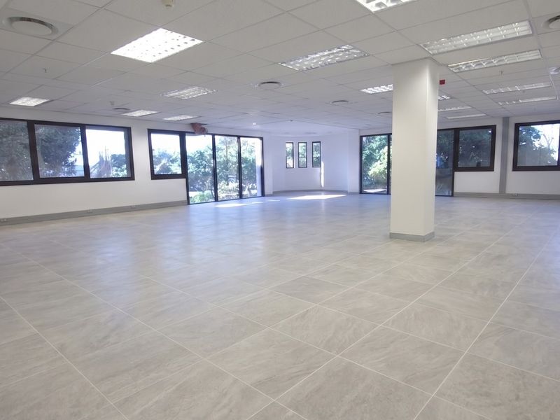 Spacious open-plan retail or office area featuring large windows, modern tiled flooring, and a suspended ceiling with recessed lighting.