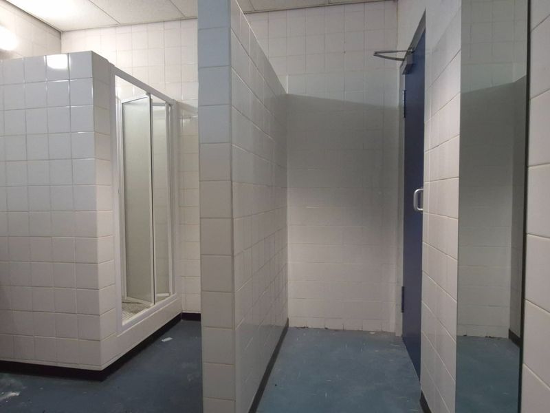 A functional bathroom space featuring tiled walls, a shower cubicle, and a wall-mounted basin, currently in need of cosmetic updates.