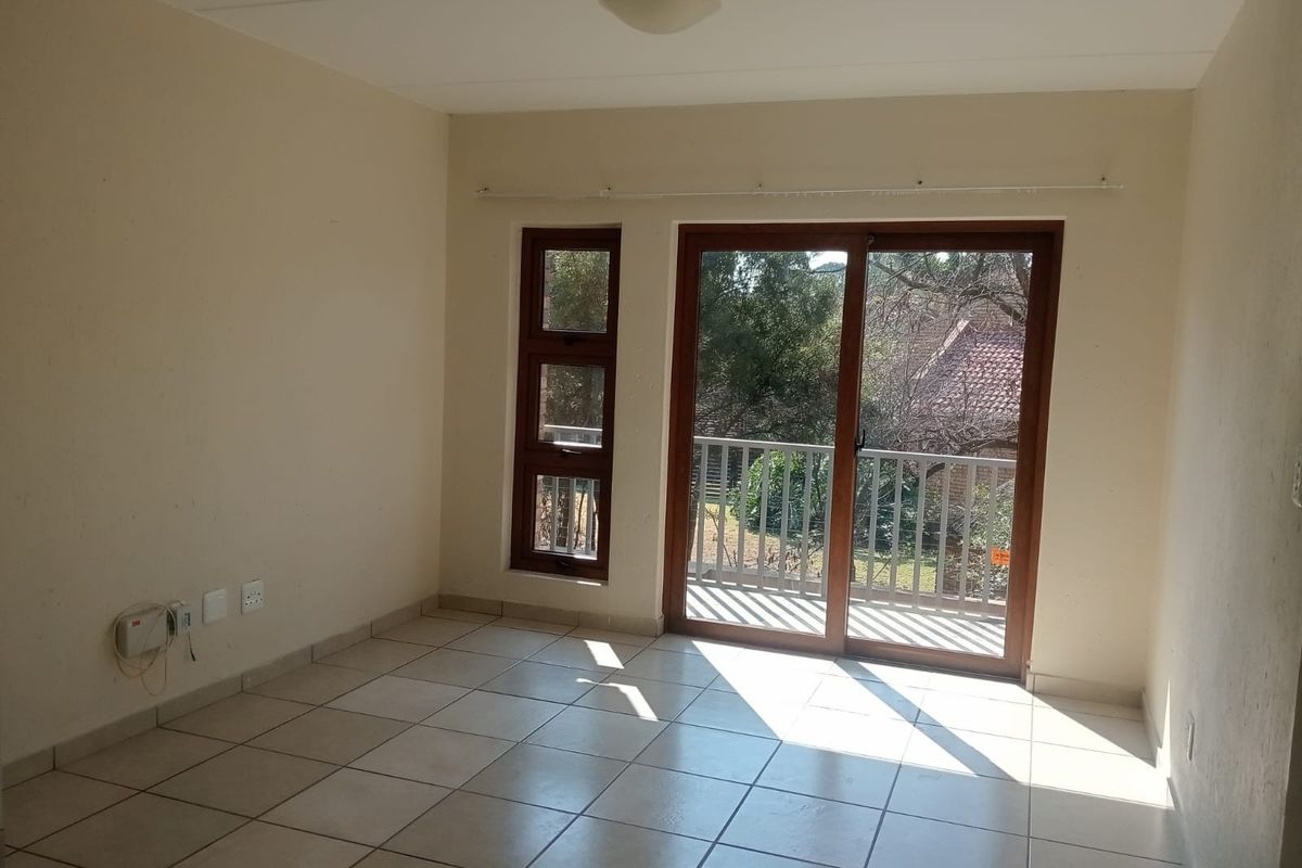 An empty living room featuring tiled flooring, neutral walls, and a sliding glass door providing access to an outdoor balcony area.
