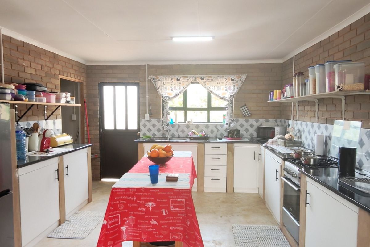 A functional kitchen featuring exposed brick walls, white cabinetry, stone countertops, and a built-in oven with hob, offering a rustic and practical workspace.