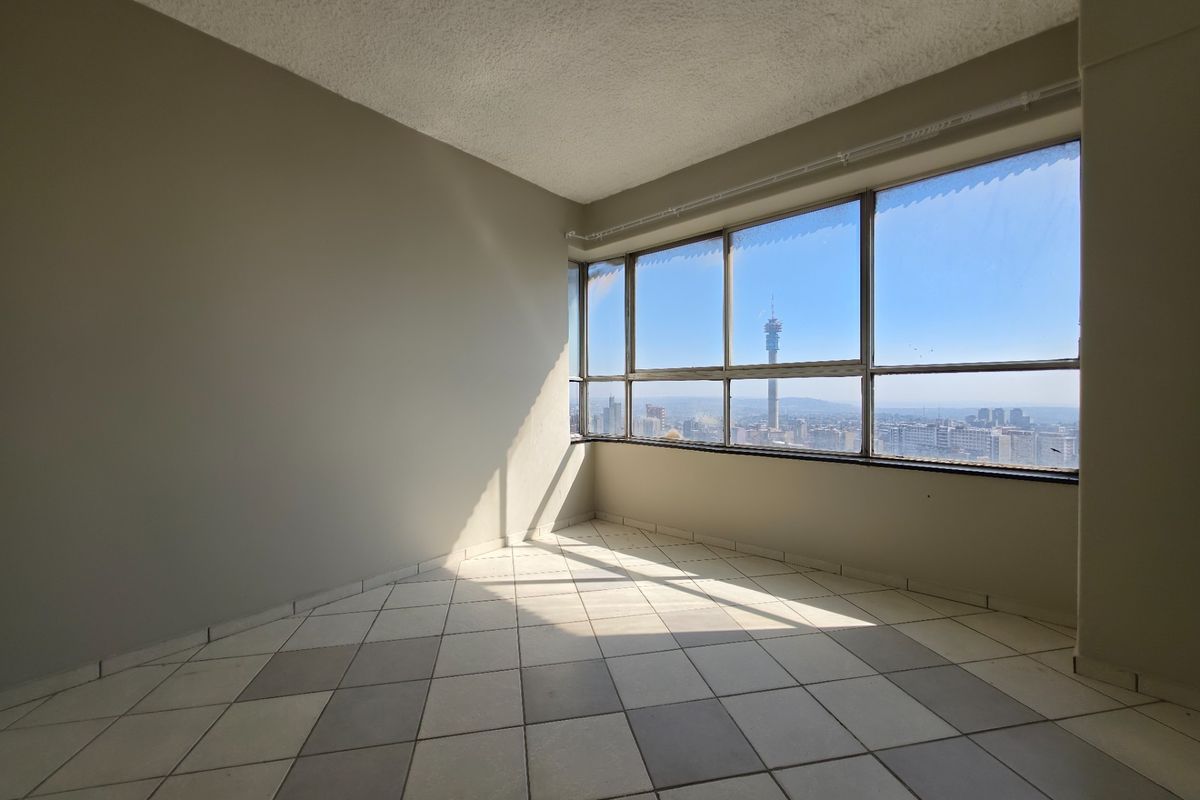 An empty living area featuring large windows with expansive city views, tiled flooring, and a textured ceiling.