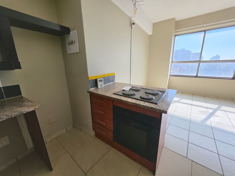 A compact kitchen area featuring built-in cabinetry, a granite countertop with an integrated electric hob and oven, and large windows providing natural light.