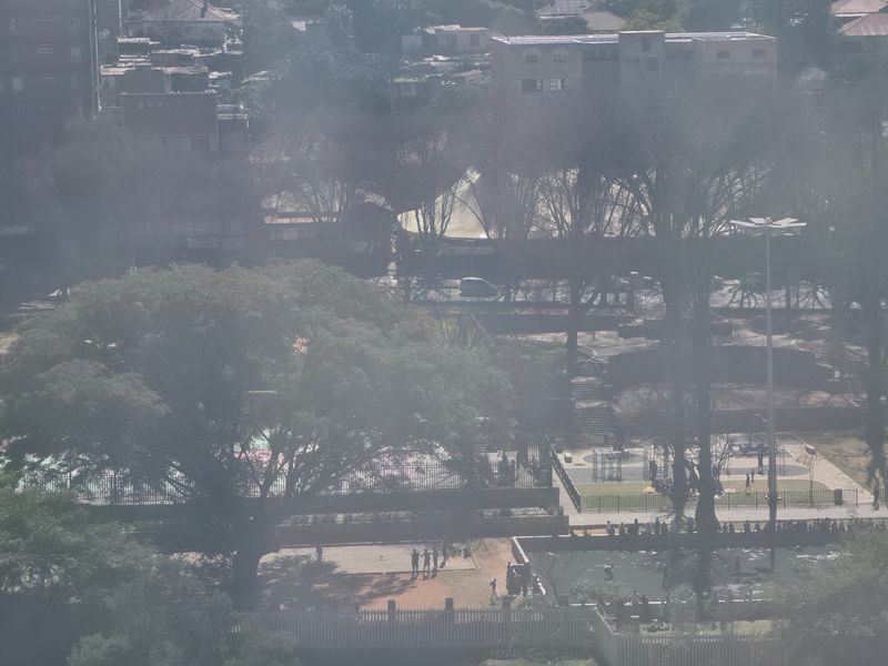 An elevated aerial view overlooking a public park area with mature trees and recreational facilities in the surrounding urban neighborhood.