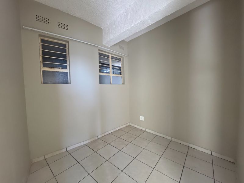 An empty bedroom featuring neutral wall paint, ceramic tiled flooring, and steel-framed windows with security bars.