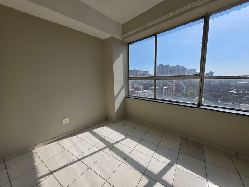 An empty bedroom featuring large windows with city views and neutral tiled flooring, offering a bright and versatile living space.