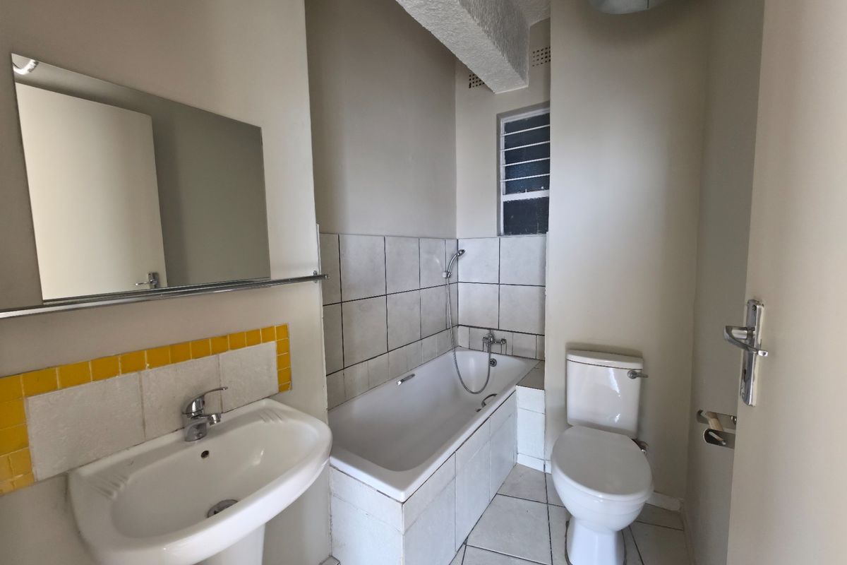 A functional bathroom featuring a pedestal basin, bathtub with shower mixer, and toilet, finished with tiled splashbacks and flooring.