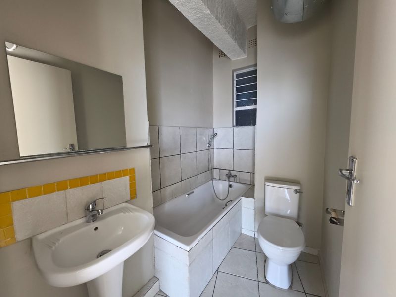 A functional bathroom featuring a pedestal basin, bathtub with shower mixer, and toilet, finished with tiled splashbacks and flooring.