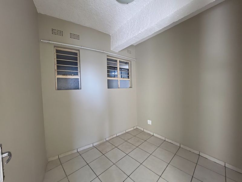An empty bedroom featuring neutral wall paint, tiled flooring, and steel-framed windows with security bars.