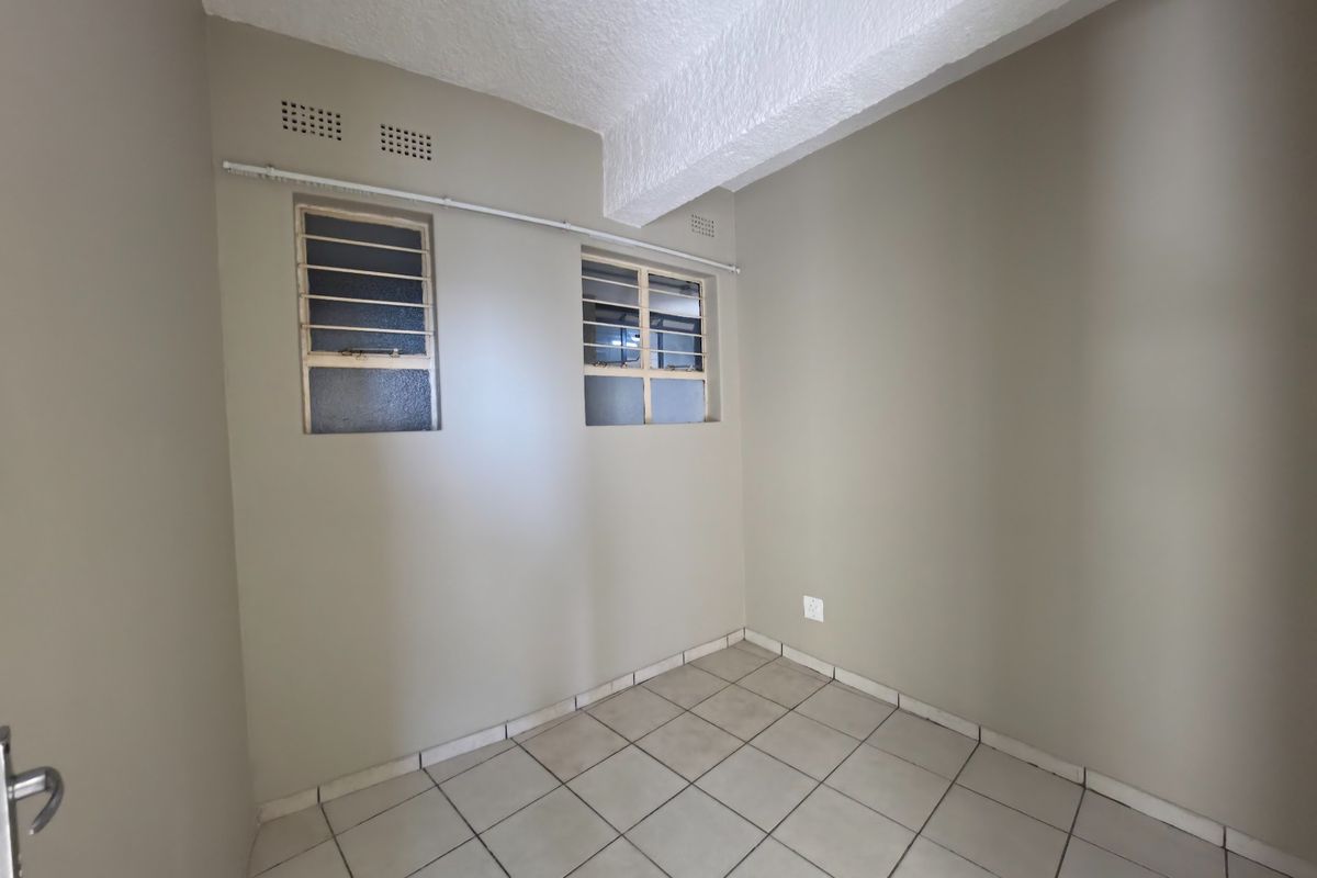 An empty bedroom featuring neutral wall paint, tiled flooring, and steel-framed windows with security bars.