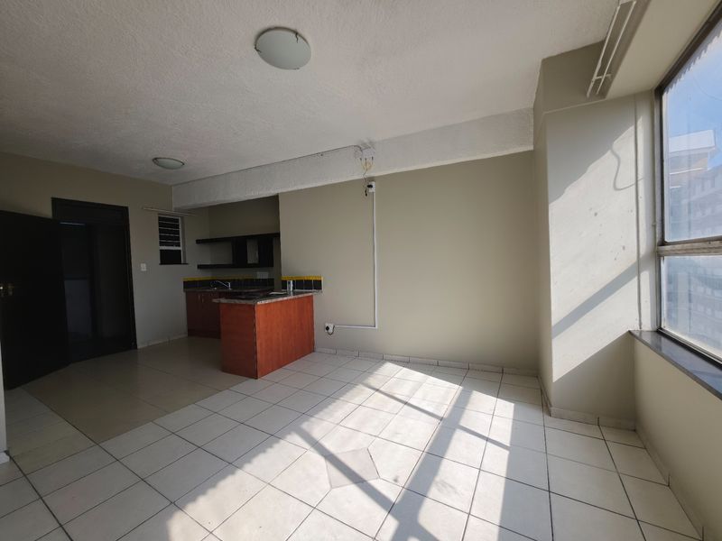 An open-plan living and kitchen area featuring tiled flooring, built-in cabinetry with granite countertops, and large windows providing natural light.