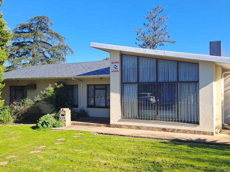 Front elevation of a mid-century style house featuring a pitched roof, large windows with security bars, and a concrete patio area.