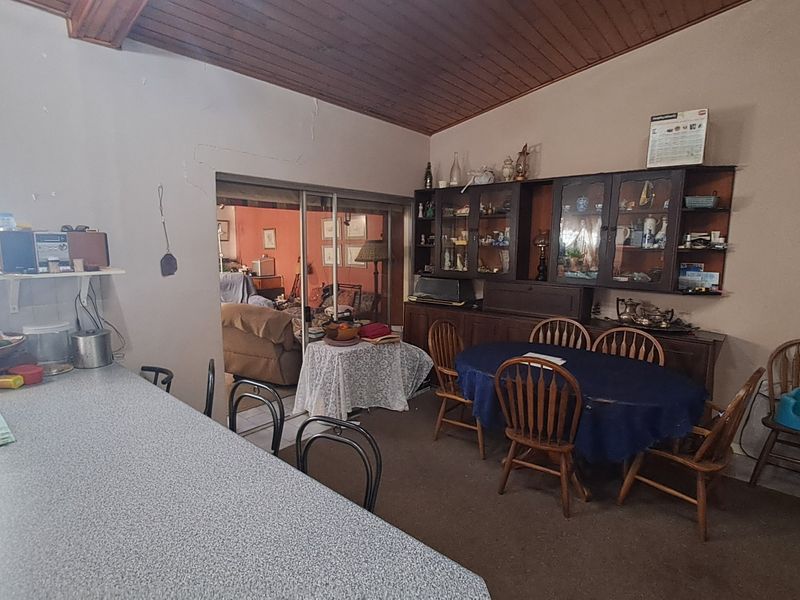 Open plan living and dining area featuring a vaulted timber ceiling, built-in display cabinetry, and a kitchen breakfast bar with access to an adjacent room.
