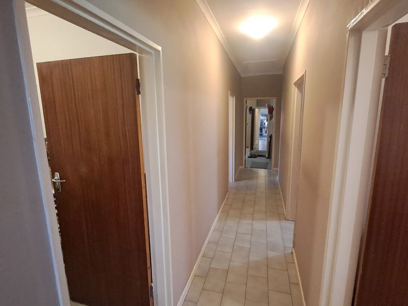 A functional hallway featuring tiled flooring, neutral wall tones, and multiple timber veneer doors providing access to adjacent rooms.