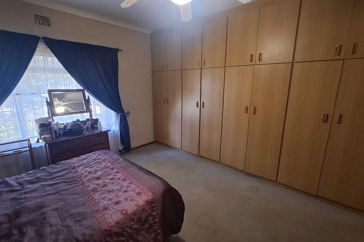 A bedroom featuring extensive floor-to-ceiling built-in wooden cupboards, a ceiling fan, and security bars on the window.
