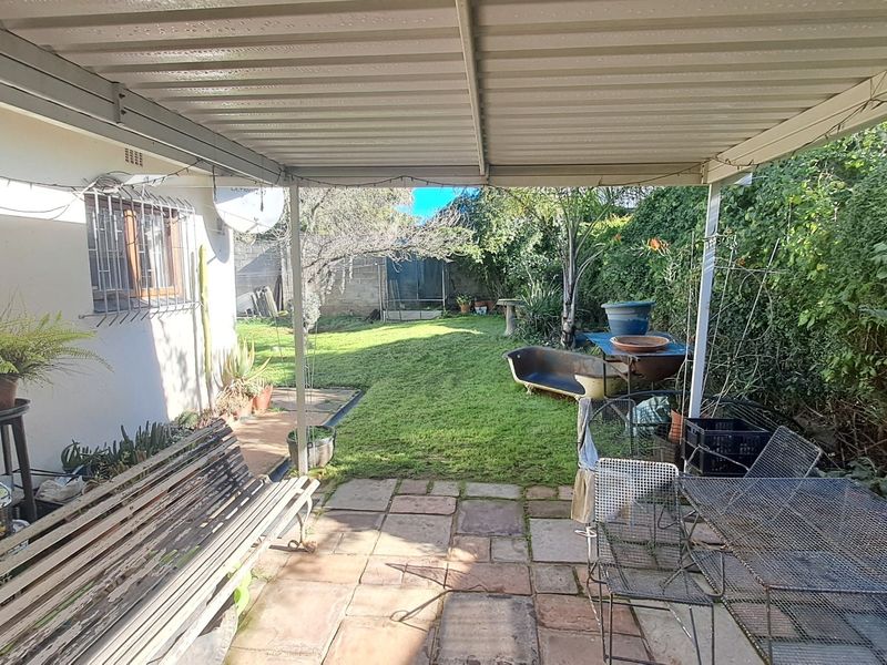 A covered patio area with paved flooring, overlooking a private garden space, providing a functional outdoor entertainment area.