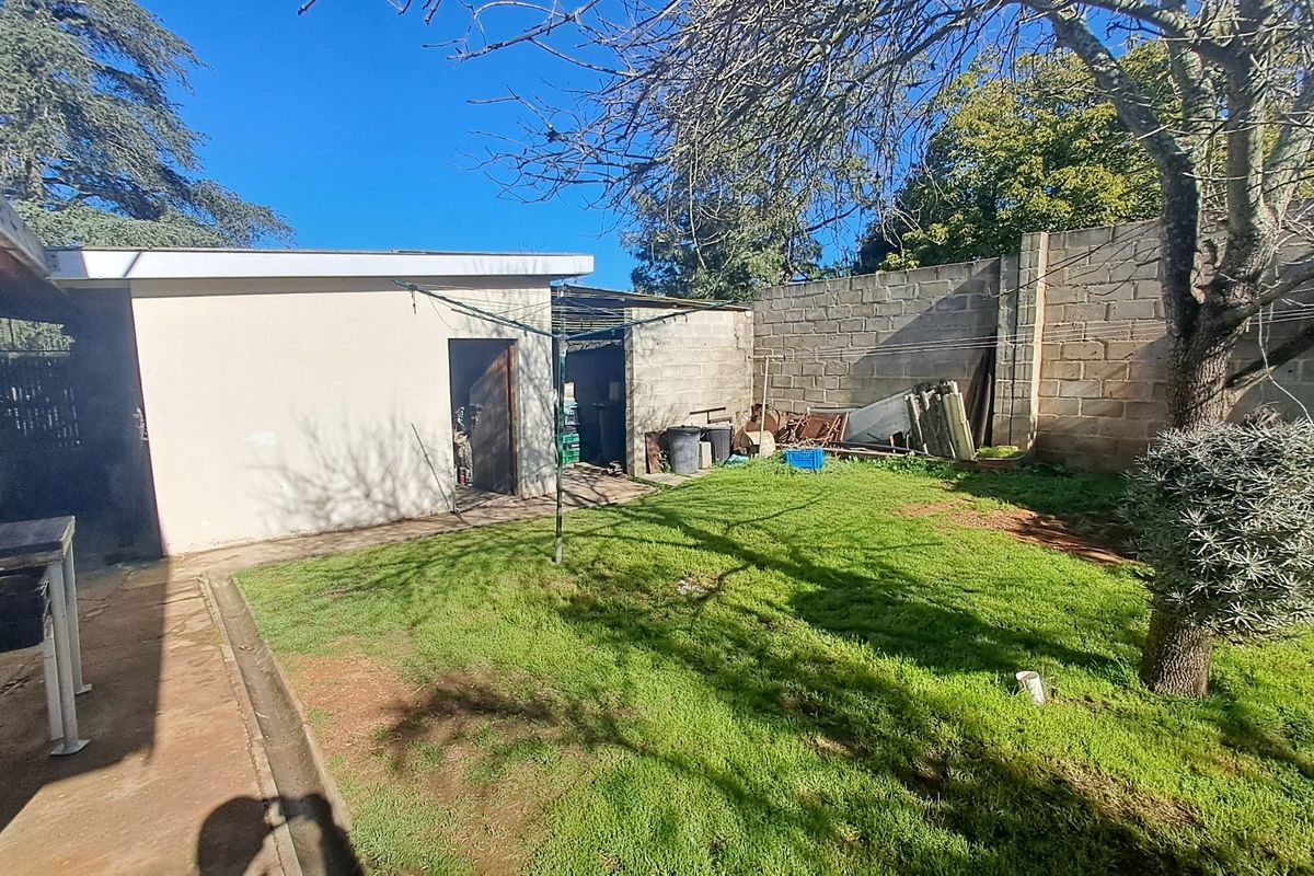 Rear garden area featuring a lawn, concrete patio, and an outbuilding, enclosed by a concrete block boundary wall.