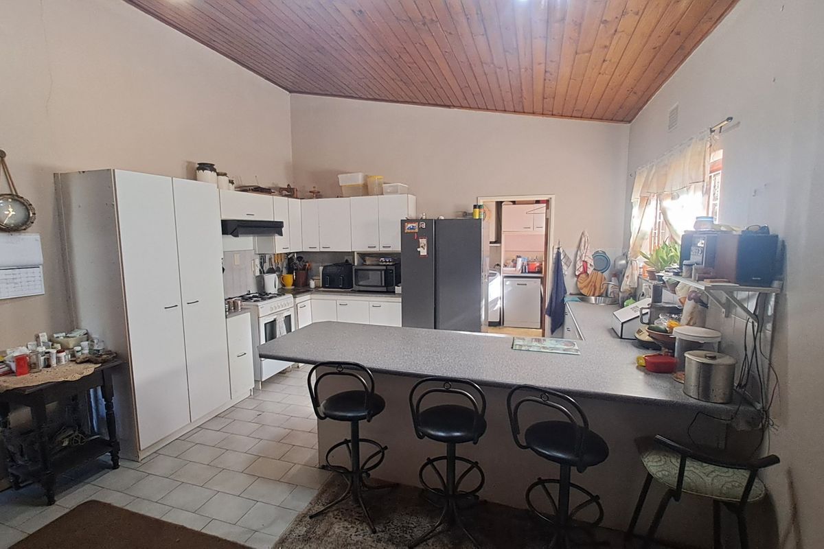 A functional kitchen featuring built-in cabinetry, a breakfast bar, and a timber-paneled ceiling, with an adjacent scullery area visible.