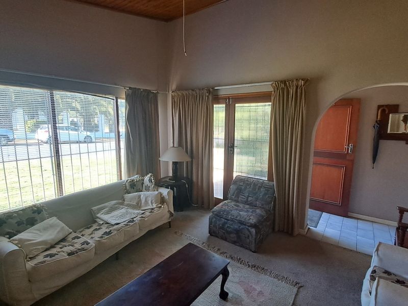 A living room featuring a timber ceiling, large windows, and an arched doorway leading to an entrance area.