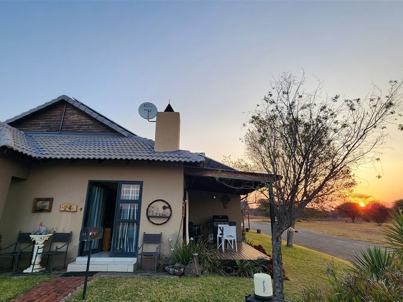 Front elevation of a single-story house featuring a tiled roof, chimney, and a covered patio area with wooden decking overlooking a scenic landscape.