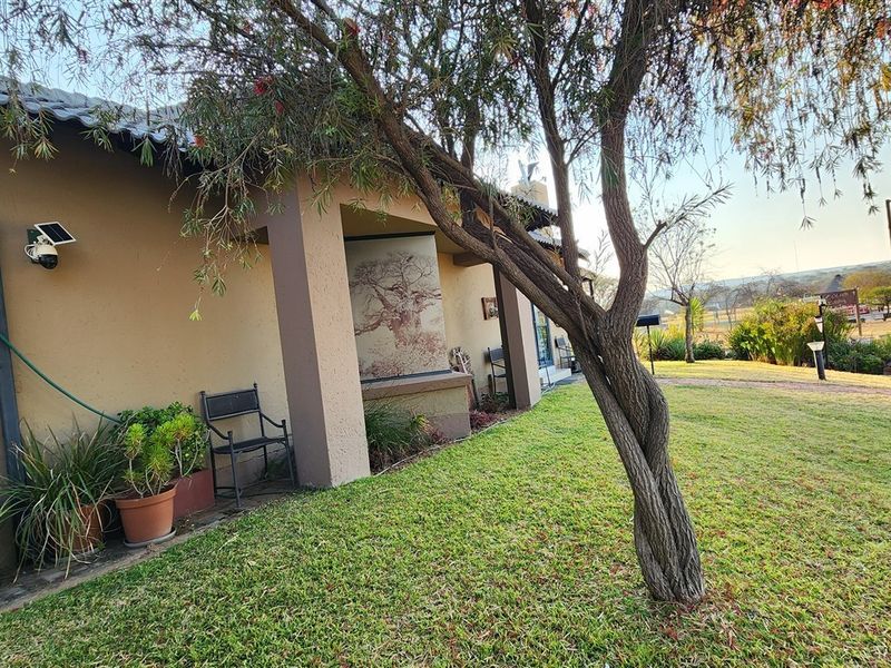 A view of the rear exterior of the house featuring a covered patio area, plastered walls, and a well-maintained garden setting.