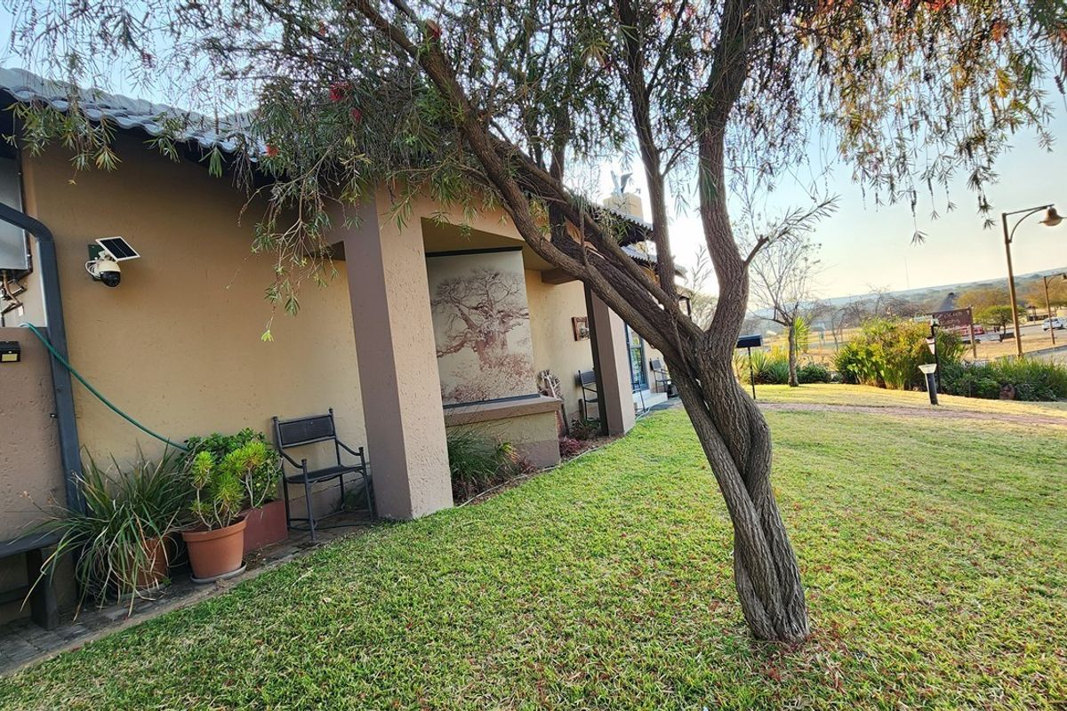 A view of the rear exterior of the house featuring a covered patio area, plastered walls, and a well-maintained garden setting.