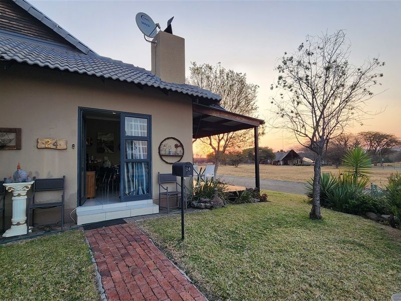 Front view of the property featuring a brick pathway, covered patio area, and a well-maintained garden setting at sunset.