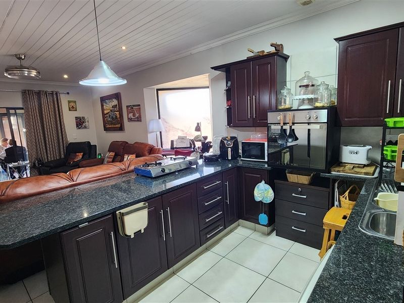 Open-plan kitchen and living area featuring dark wood cabinetry, granite countertops, tiled flooring, and a tongue and groove ceiling.