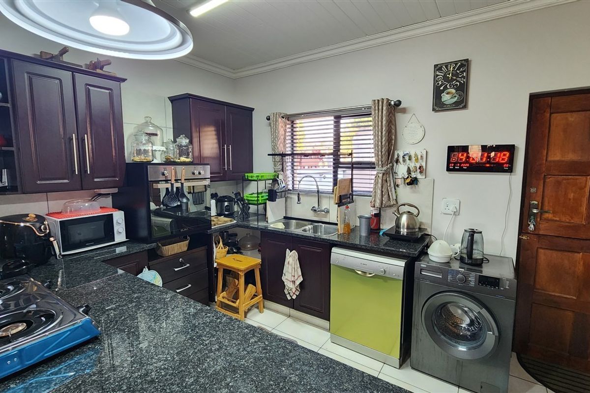 A functional kitchen featuring dark wood cabinetry, granite countertops, a double bowl sink, and built-in oven, with tiled flooring and a timber door.