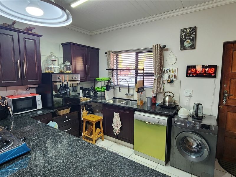 A functional kitchen featuring dark wood cabinetry, granite countertops, a double bowl sink, and built-in oven, with tiled flooring and a timber door.