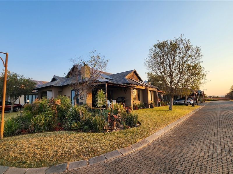 A well-maintained single-story house featuring a tiled roof with solar panels, a covered patio, and a landscaped front garden along a paved street.