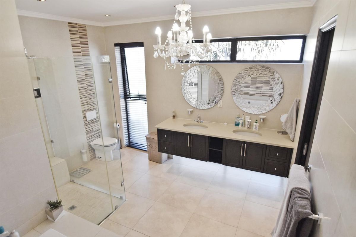 Modern bathroom featuring a double vanity with stone countertop, glass-enclosed shower, wall-mounted toilet, and elegant chandelier lighting.
