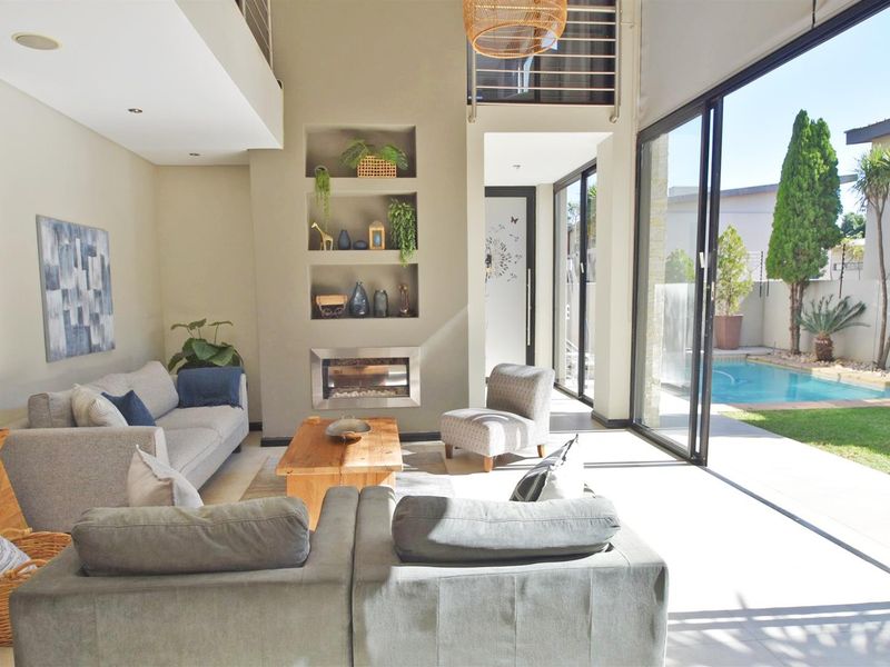 Spacious living room with high ceilings, built-in fireplace, recessed shelving, and large sliding glass doors opening to a private pool and garden area.